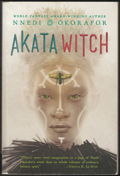 Front cover of Akata Witch by Nnedi Okorafor, featuring a face with white markings and a green insect on the forehead, with the title in large teal and red lettering.