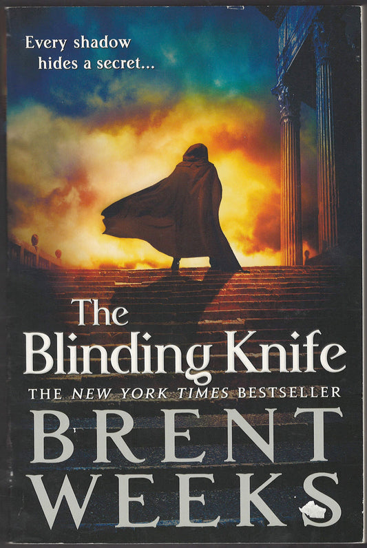 Front cover of The Blinding Knife by Brent Weeks with a silhouette of a cloaked figure walking up stairs into a fiery sky.
