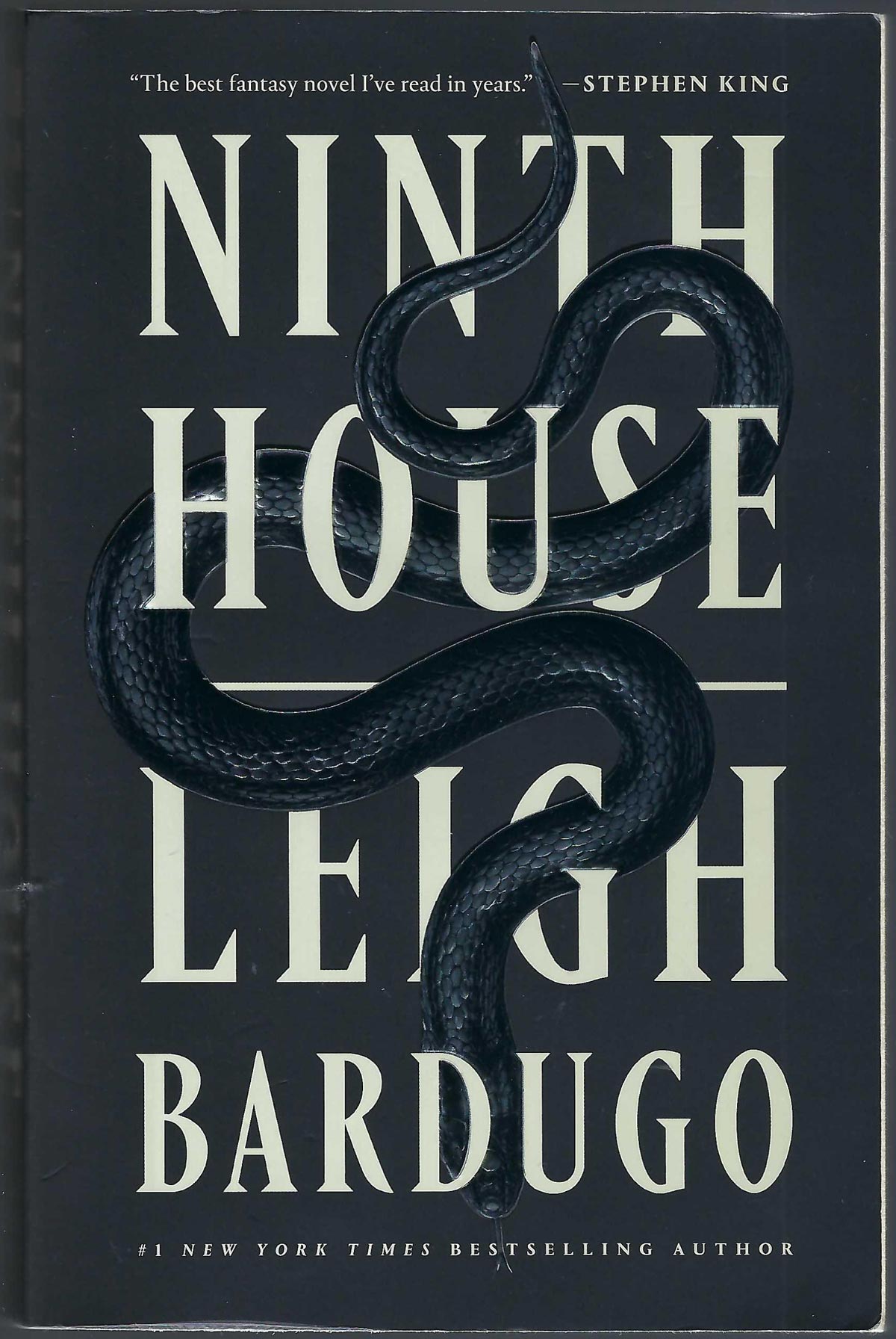 Front cover of Ninth House by Leigh Bardugo, featuring a dark black background with large cream-colored title and a coiled black snake running through the text.